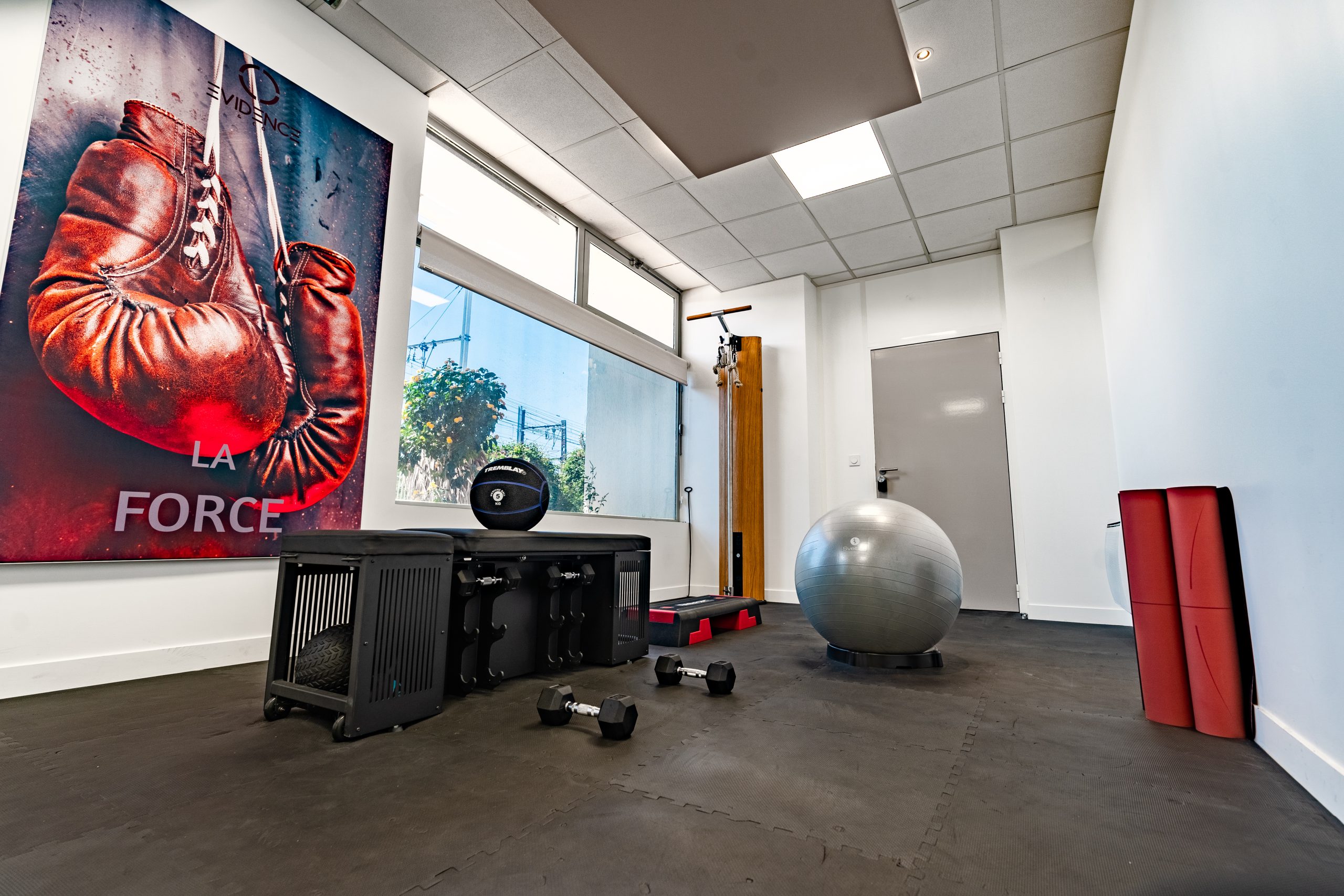 Salle de fitness lumineuse avec affiche de gants de boxe, ballon de stabilité, et divers équipements d'entraînement.